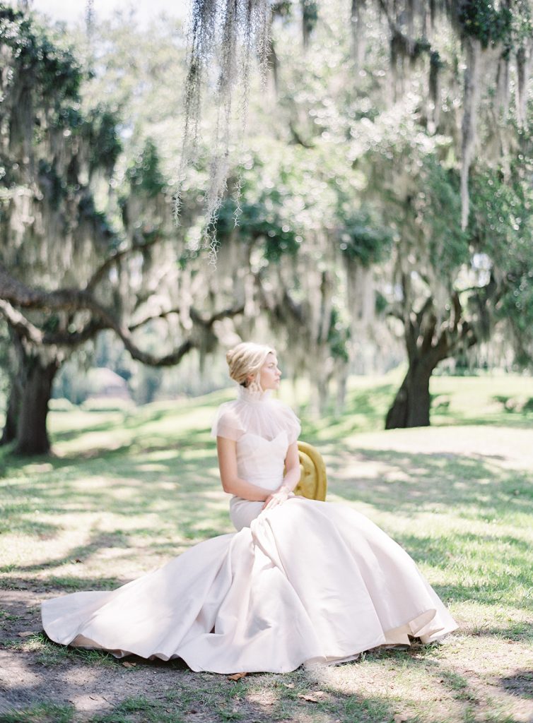Bride in a strapless thick satin ivory wedding gown designed by Anne Barge. Bride is  sitting on a golden chair in the middle of old oak trees with draping spanish moss. Photographed by wedding photographers in Charleston  Amy Mulder Photography.