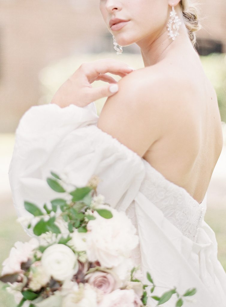 Bride in an ivory wedding gown and ivory wedding cape that starts middle of her upper arm and has puffed sleeves. Designed by Anne Barge and photographed by wedding photographers in Charleston Amy Mulder Photography.