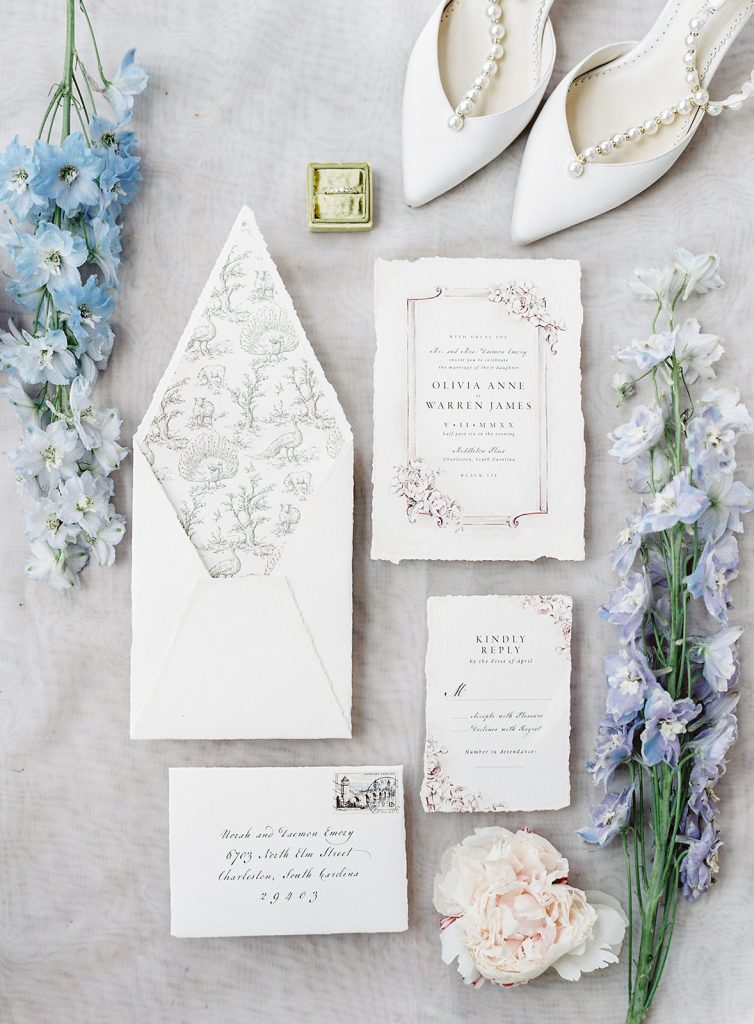 Hand drawn and hand painted custom wedding invitation suite. All ivory with tanned edging on handmade paper with hand painted florals and peacock, moss colored hand drawn peacocks, oak trees and sheep on the lining of the envelope. Photographed by wedding photographers in Charleston Amy Mulder Photography. 