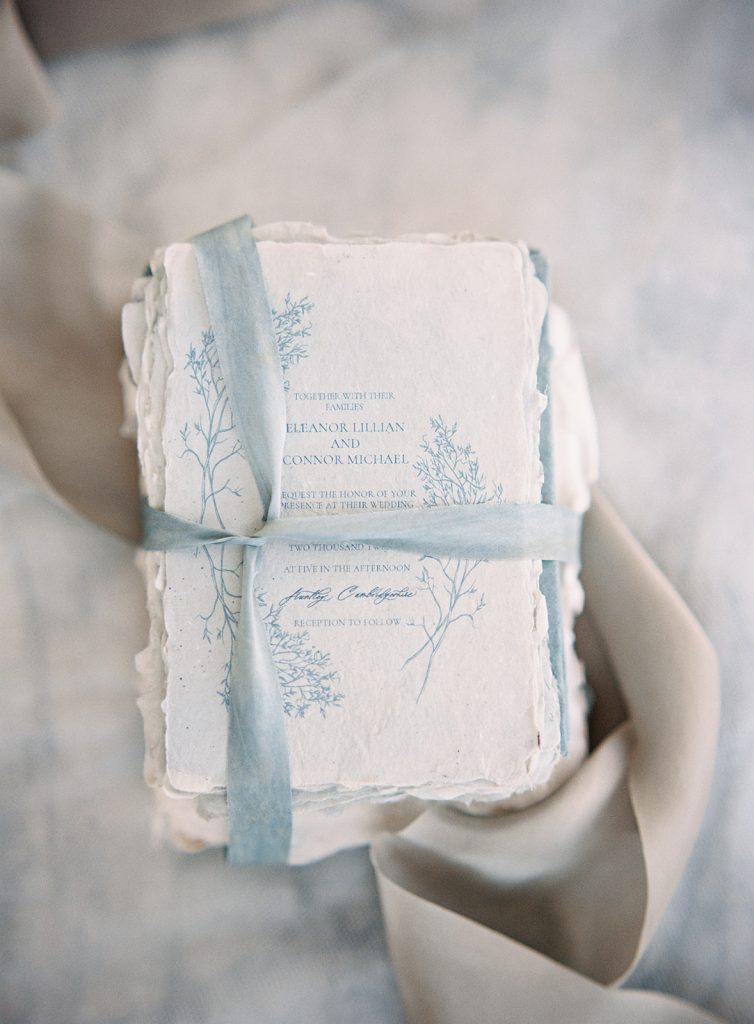 A tall stack of ivory handmade paper wedding invitations with light blue floral and words letter pressed on. Photographed by wedding photographers in Charleston Amy Mulder Photography.