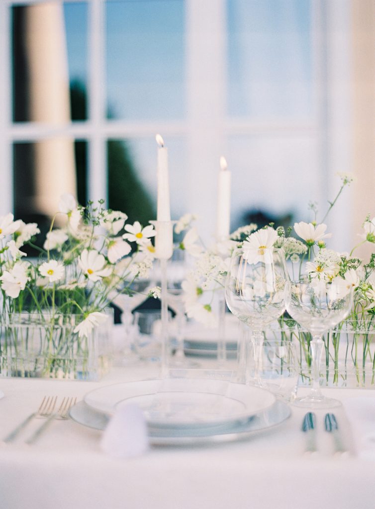 Wedding reception table with white linens, plates and candles in glass candlesticks. All clear glass wine and cocktail glasses and custom made vases with white flower stems creating the centerpieces. Photographed at destination wedding in Italy by wedding photographers in Charleston Amy Mulder Photography. 