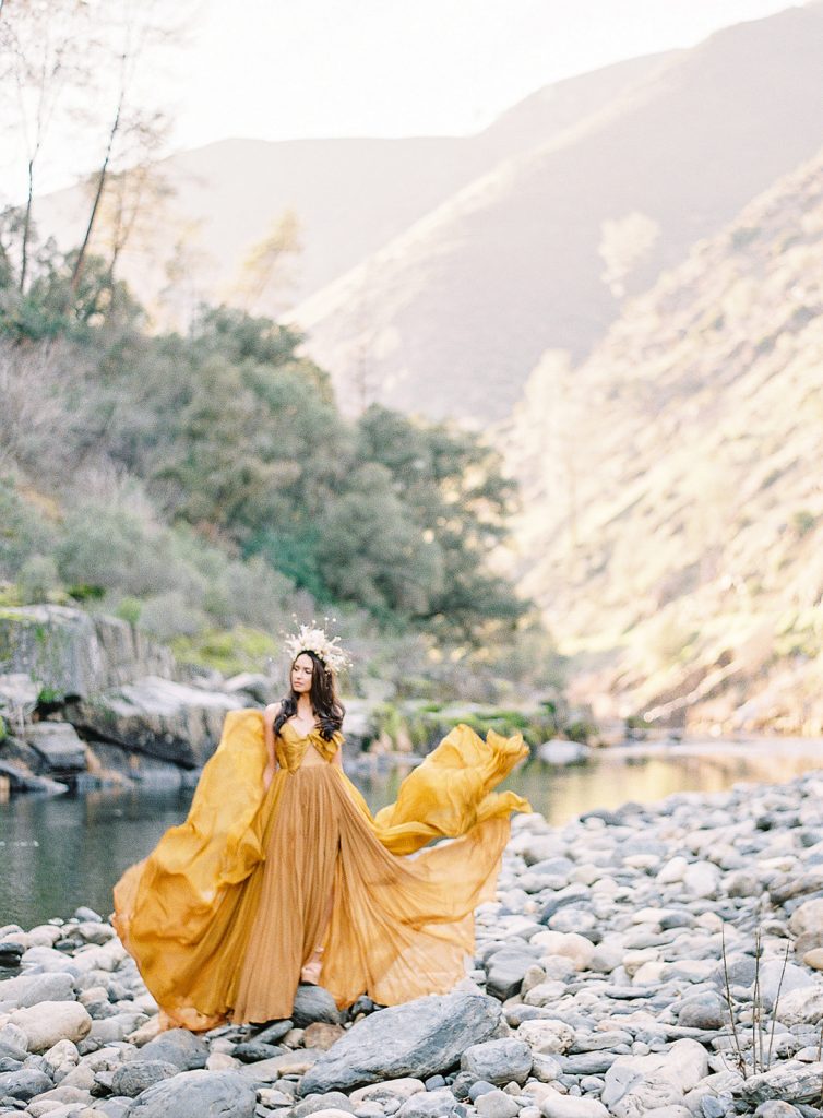 Model in yellow gown of layer and layers catching in the wind around her. She is on rocks in a valley. Photographed at destination wedding by wedding photographers in Charleston Amy Mulder Photography.