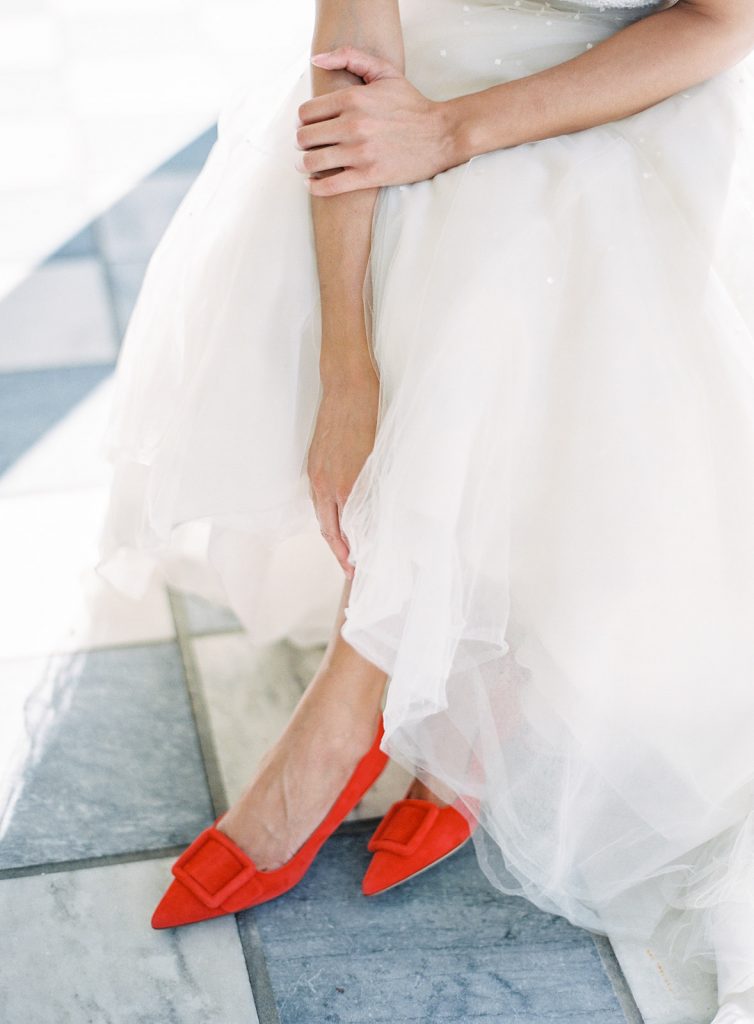 Bride with her arms draping down her legs and ending by her red Manolo Blahnik shoes. Photographed at the William Aiken House wedding by wedding photographers in Charleston Amy Mulder Photography,