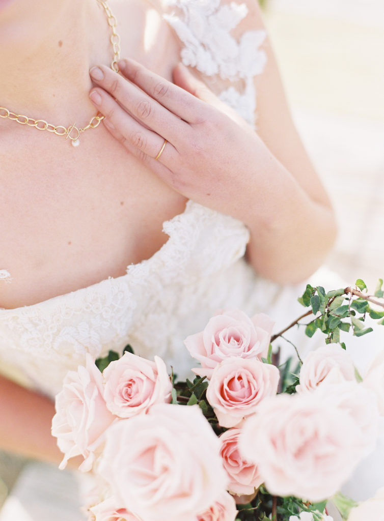Close up of bride's gold band wedding ring by her gold necklace with a single pearl. Bride is in detailed gown with blush wedding bouquet. Lowndes Grove wedding photographed by wedding photographers in Charleston Amy Mulder Photography.