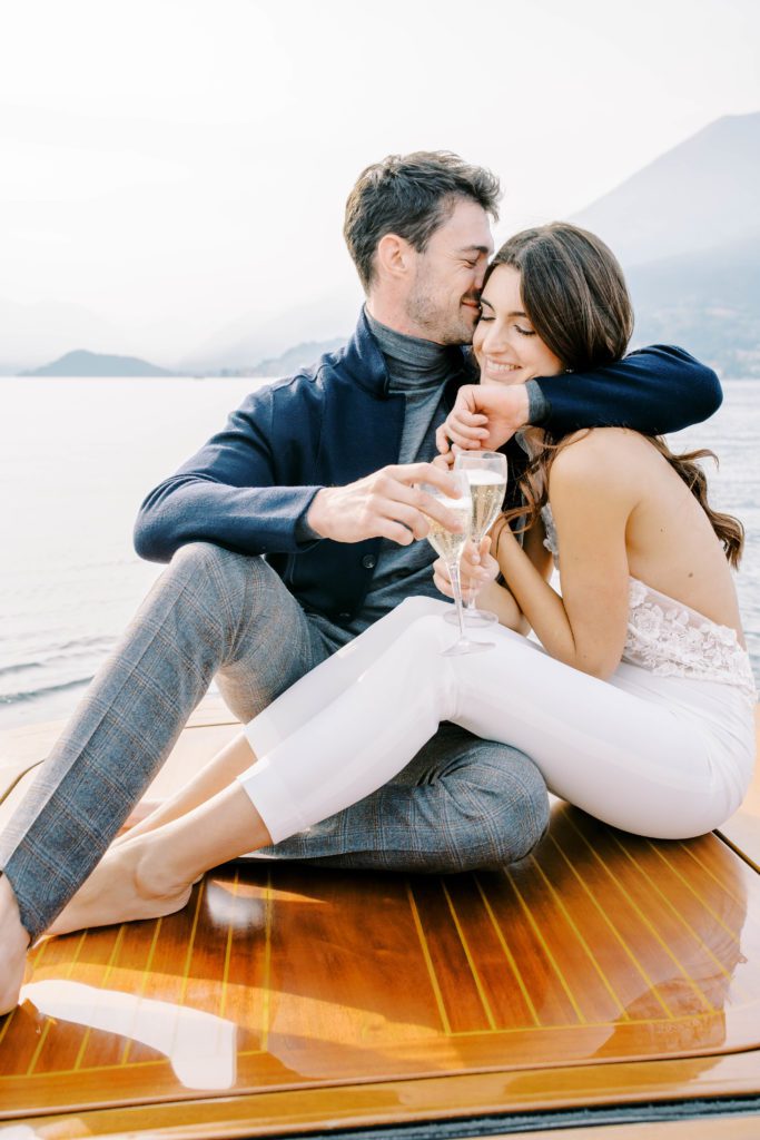 Couple on back of luxury boat from Grand Hotel Tremezzo drinking prosecco and laughing.  Photographed by Italy Wedding Photographer, Amy Mulder Photography.