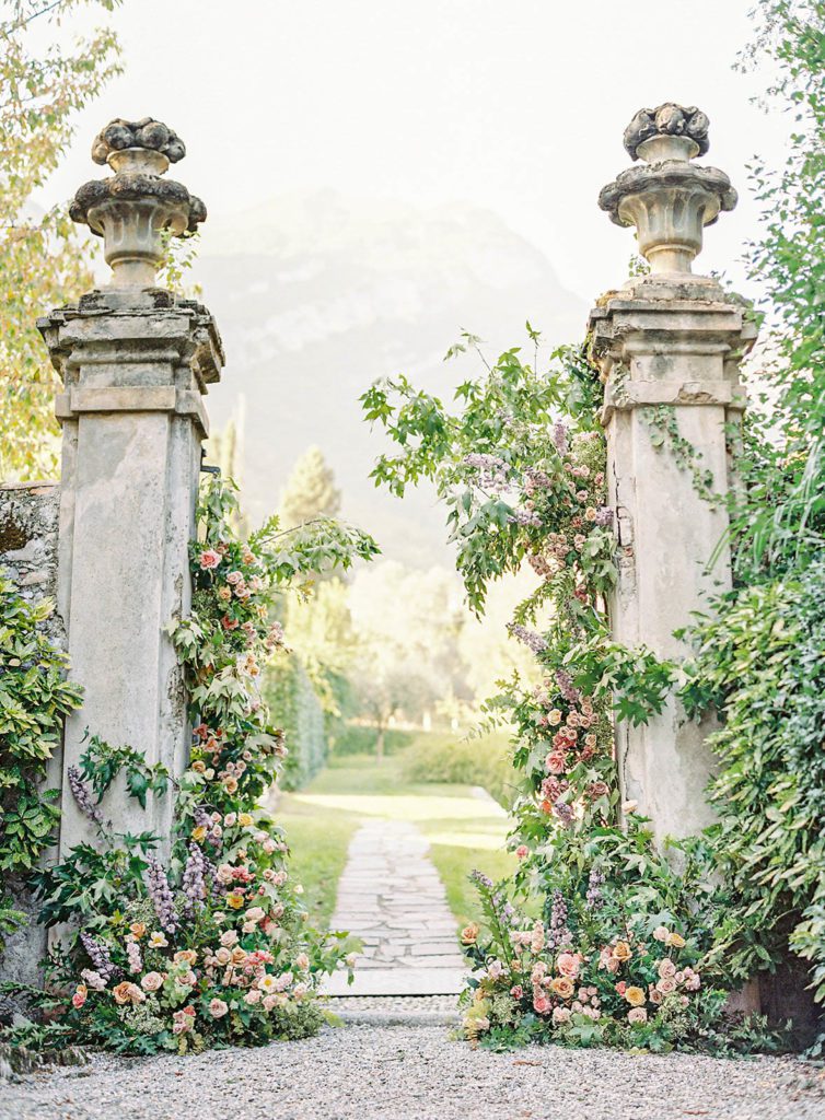 Villa Sola Cabiati Luxury wedding. Photographed by Italy wedding photographer, Amy Mulder Photography. Bride on stairs inside the villa. Back of the villa in the gardens where two large columns are covered in greenery and flowers for ceremony site. 