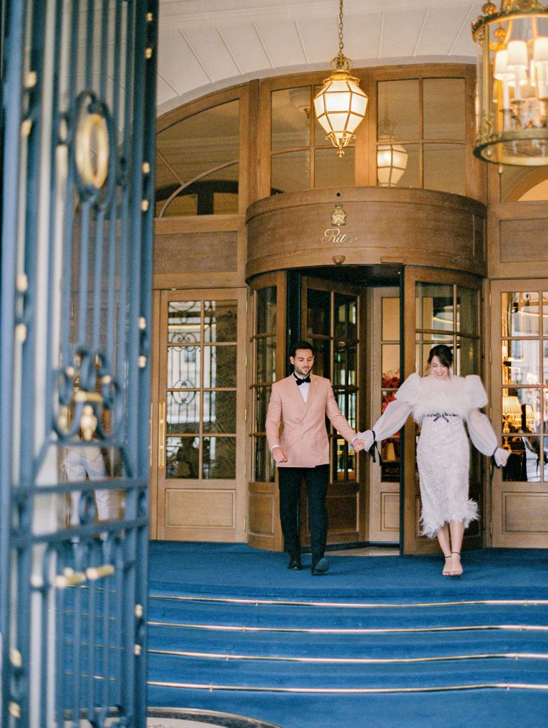 Bride and groom leaving Ritz Paris in tea length white feather and lace dress and groom in peach dinner jacket.