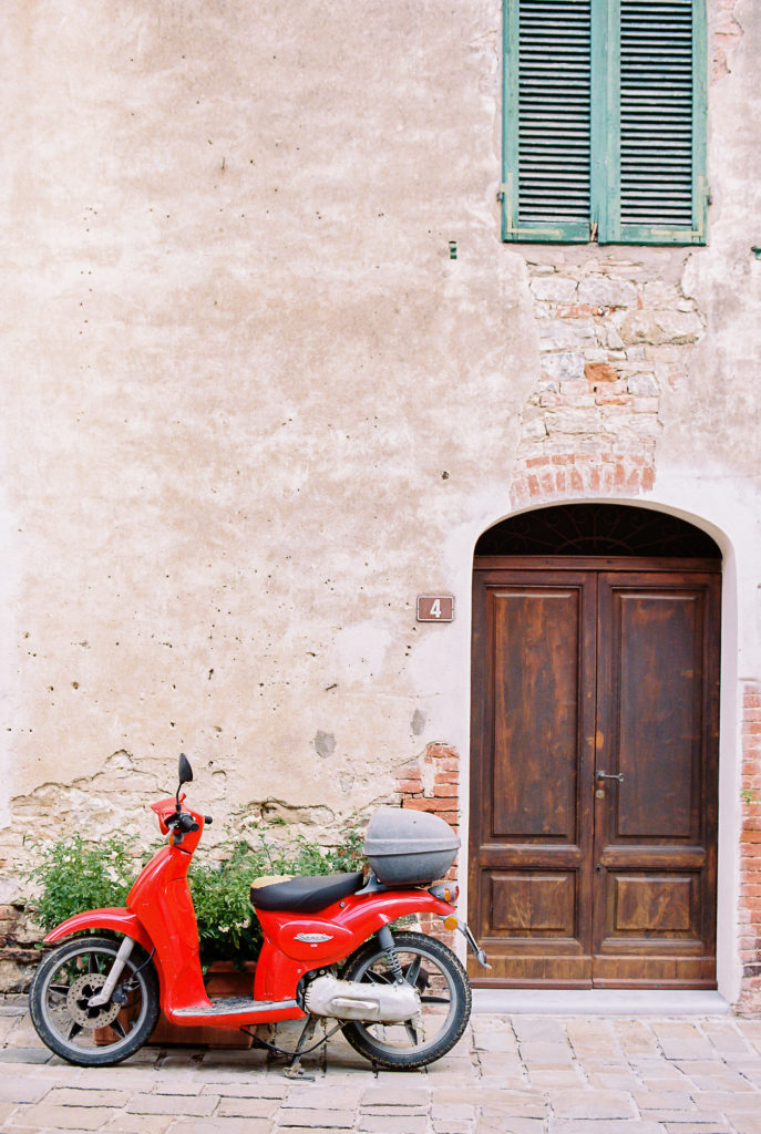 Red vespa outside a brick and stucco home in Tuscany Italy