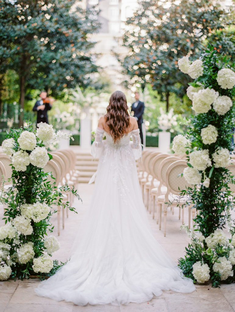 Bride from the back as she walks down the aisle of a wedding ceremony at the Ritz Paris