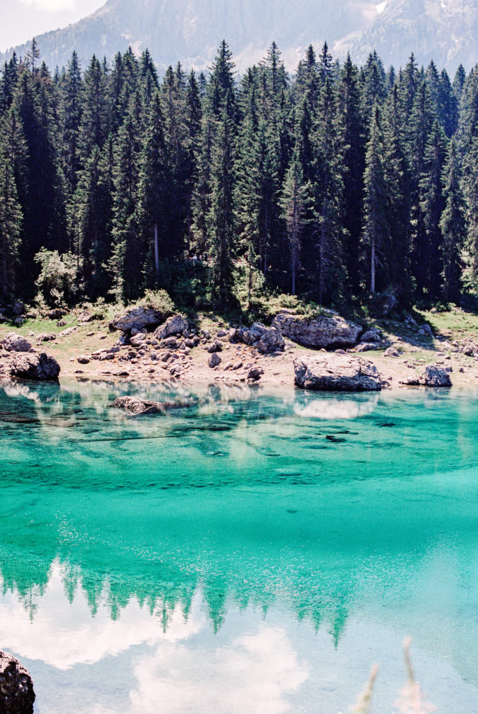 Lake Carezza in the Dolomites. Teal clear water with reflections of the pines and mountains.