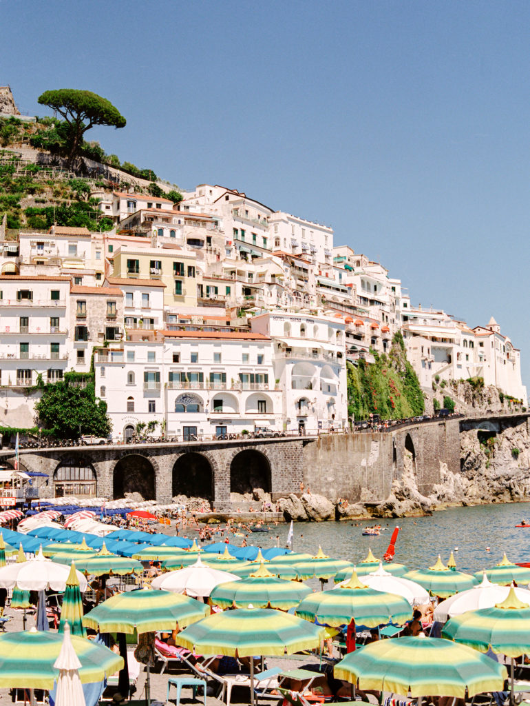 The town of Amalfi with beach front lined with green and yellow umbrellas 