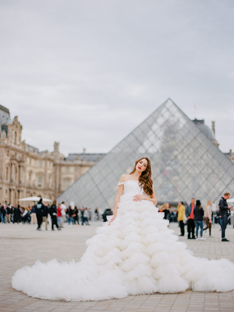 Destination wedding in Paris with bride in off the shoulder gown in front of the glass triangle at The Louvre.