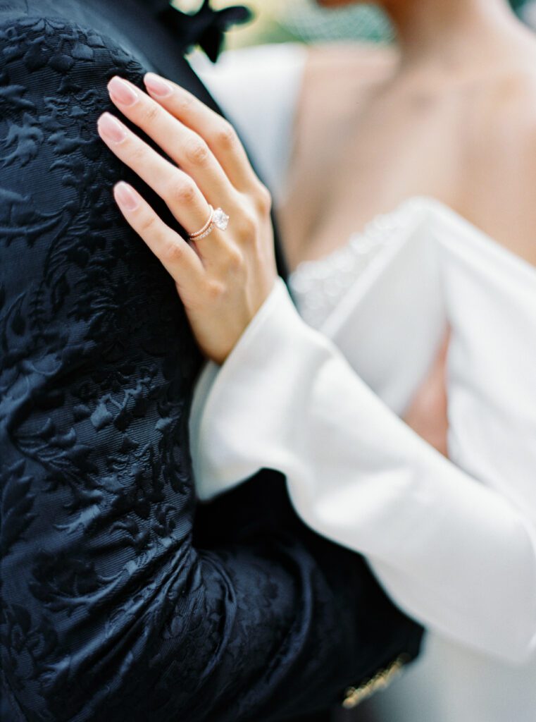 Groom in custom made textured black tuxedo embracing his wife in an off the shoulder wedding gown with buttons down the sleeves and pearls adorning the back for an intimate wedding on Lake Como in Italy photographed on film by Lake Como wedding photographer