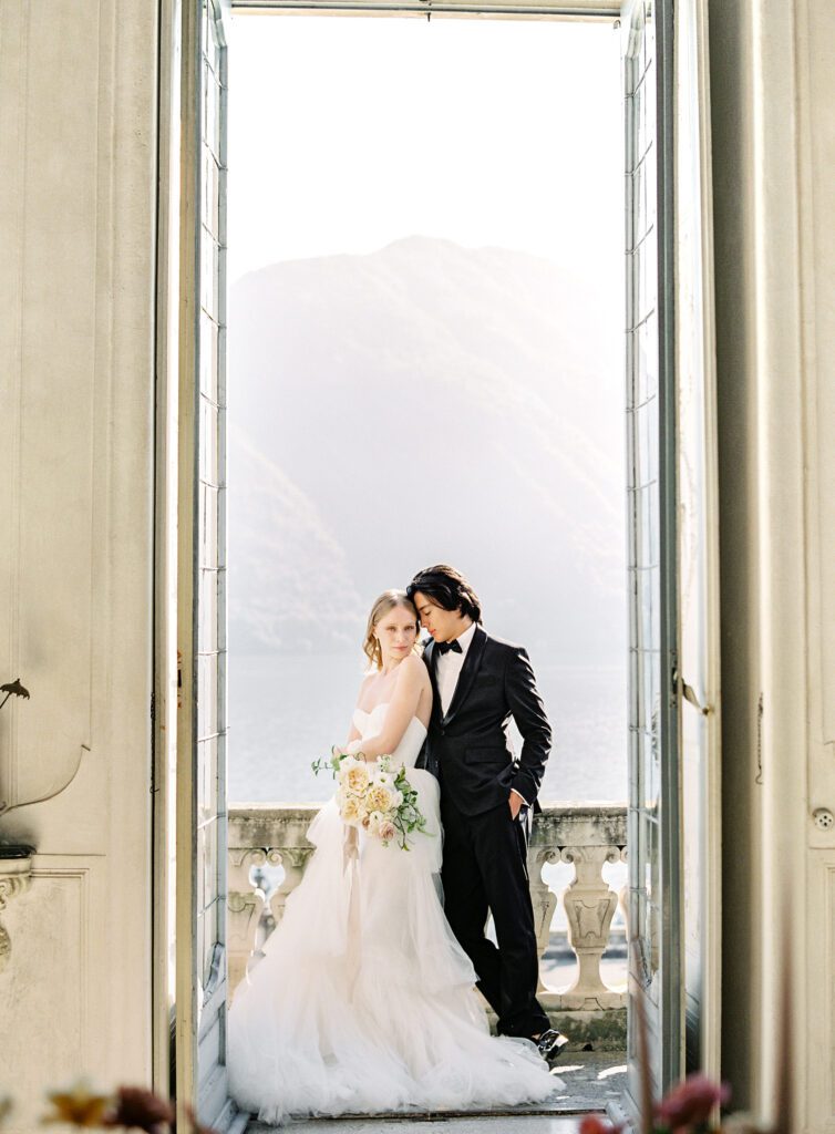 Bride and groom inside Villa Sola Cabiati with views of the lake and mountains in the background on
 their wedding day at Villa Sola Cabiati on Lake Como in Italy photographed on film by Lake Como wedding photographer