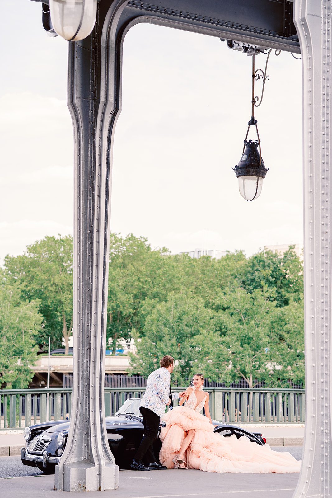 A Paris Engagement Session with vintage black convertible, couple in formal attire, he in black dress trousers and floral patterned dinner jacket and she in a hi-low peach deep v neck and multi tiered gown photographed on film in Paris by Italy Wedding Photographer