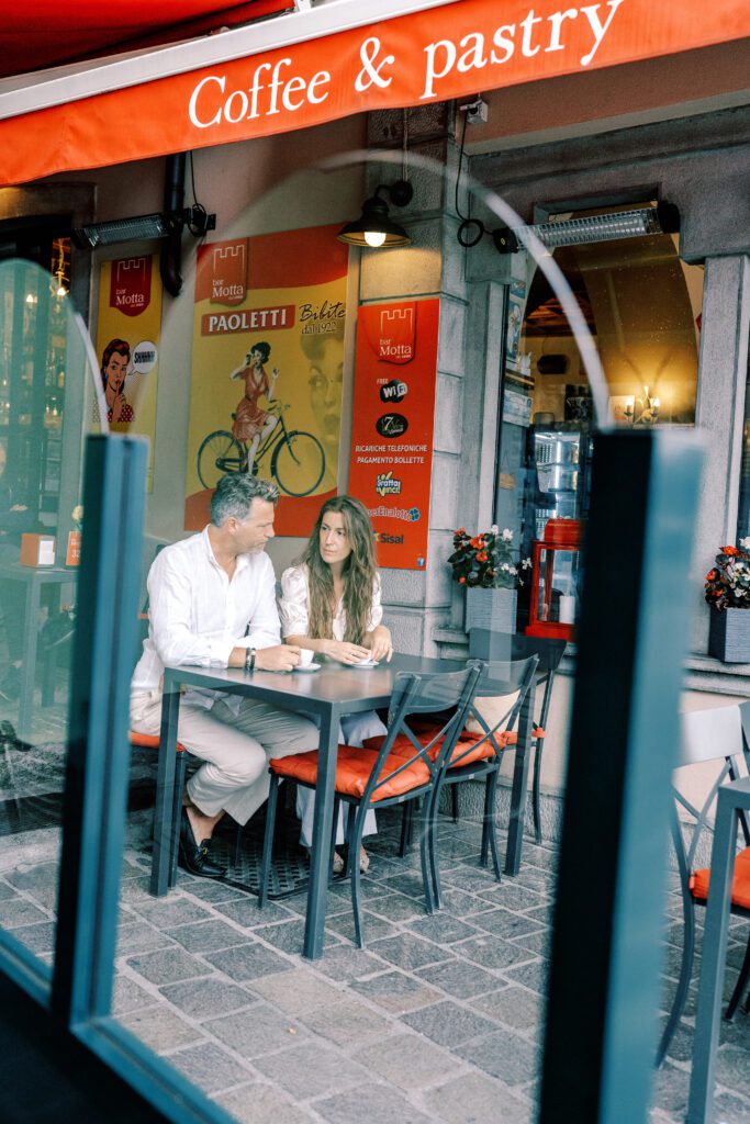 Lake Como vacation session in Argegno at cafe enjoying espresso, laughing and holding hand photographed by Lake Como photographer